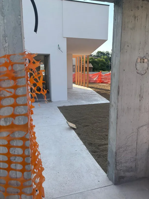 Portico con pilastri in legno e camminamento esterno finito, visto da un'apertura al grezzo